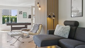 En moderne stue med et billardbord, en grå sofa og en lænestol.