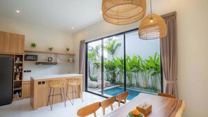 A modern kitchen with a central island, bar stools, and a dining table with a centerpiece. - Villa Mallorca Ubud (Ubud)