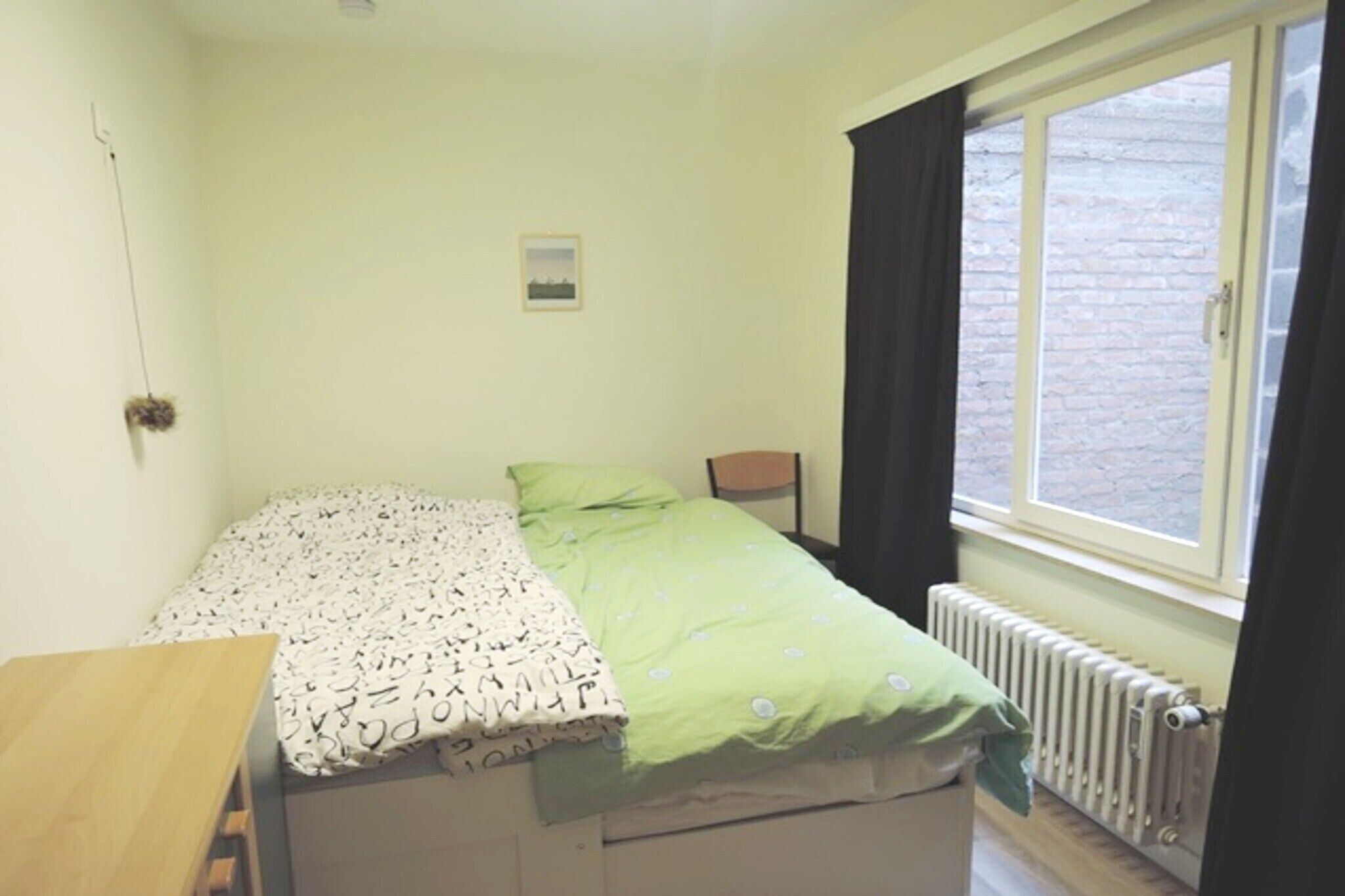 A small, single-bed room with a window, a radiator, and a small table.