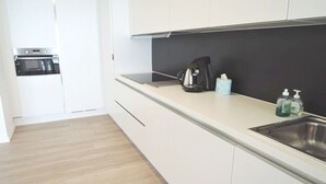 Una cocina moderna con armarios blancos, una cafetera negra y un lavamanos de acero inoxidable.