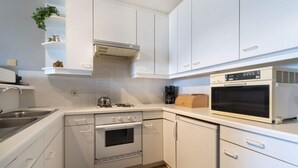 A compact kitchen with white cabinets, a stove, oven, microwave, and a coffee maker.