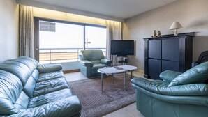 A hotel room with a large window, a flat-screen TV, a sofa, a chair, and a cabinet.