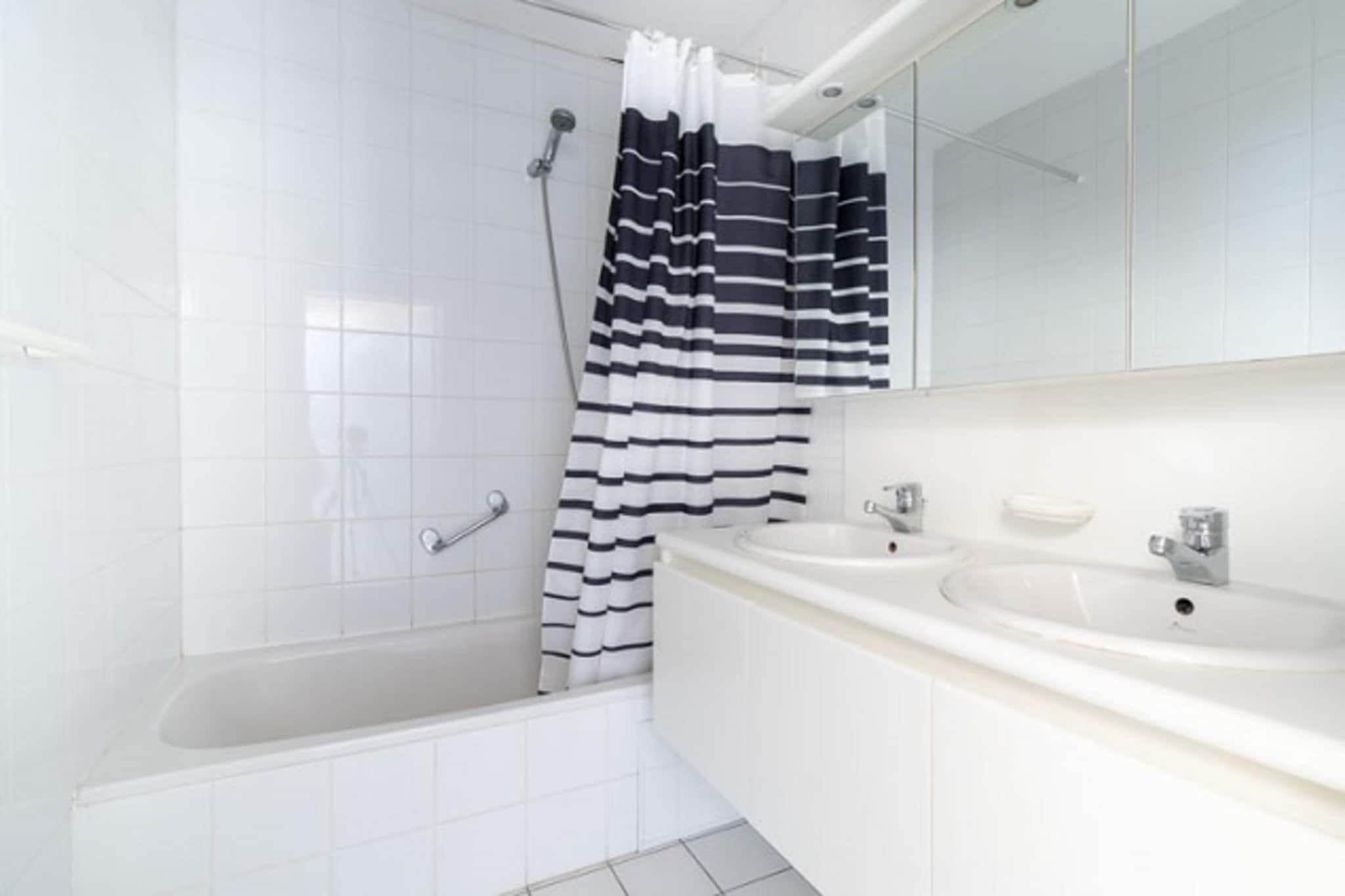 Une salle de bain moderne avec une baignoire, deux lavabos et un rideau de douche à rayures.