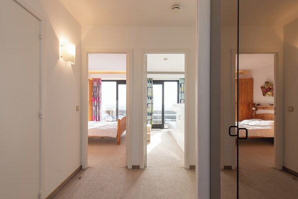 A hotel corridor with two bedrooms, each with a bed and a nightstand.