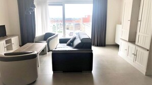Ein modernes Wohnzimmer mit einer Couch, Hocker und einem Fernseher auf einem Schrank.