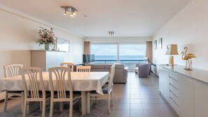Habitación de hotel moderna con zona de comedor, sofá, televisión y vista al mar.