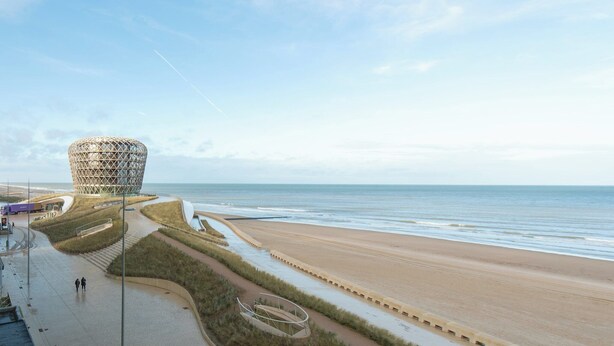Vista costera con un edificio circular distintivo cerca de la playa, un sendero pavimentado y el océano.