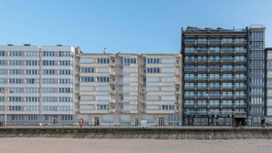 Un hôtel à plusieurs étages doté de balcons, une plage de sable en premier plan et un ciel dégagé.