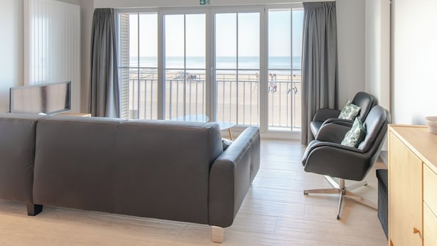 Une chambre d’hôtel moderne dotée d’une grande porte-fenêtre coulissante donnant sur un balcon avec vue sur la plage.