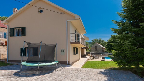 A two-story house with a trampoline in the backyard, a pool, and a small garden.