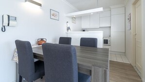 Eine moderne Küche mit weißen Schränken, einer zentralen Kochinsel und einem Essbereich mit Holztisch und vier Stühlen.
