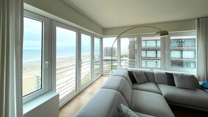 Un salon moderne doté d’une grande fenêtre donnant sur une plage et offrant une vue sur le paysage urbain.