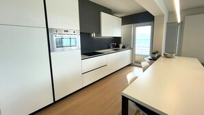Une cuisine moderne avec des meubles blancs, un four encastré et un grand îlot central doté d’un évier.