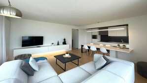 Un salon moderne avec un canapé, une table basse et un téléviseur. Il y a également un coin cuisine avec une table à manger et des chaises.
