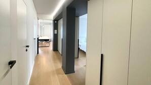 Un couloir moderne avec un plancher en bois, des murs blancs et un mur d’accent noir. On y voit des portes sur la gauche et un lit au fond.