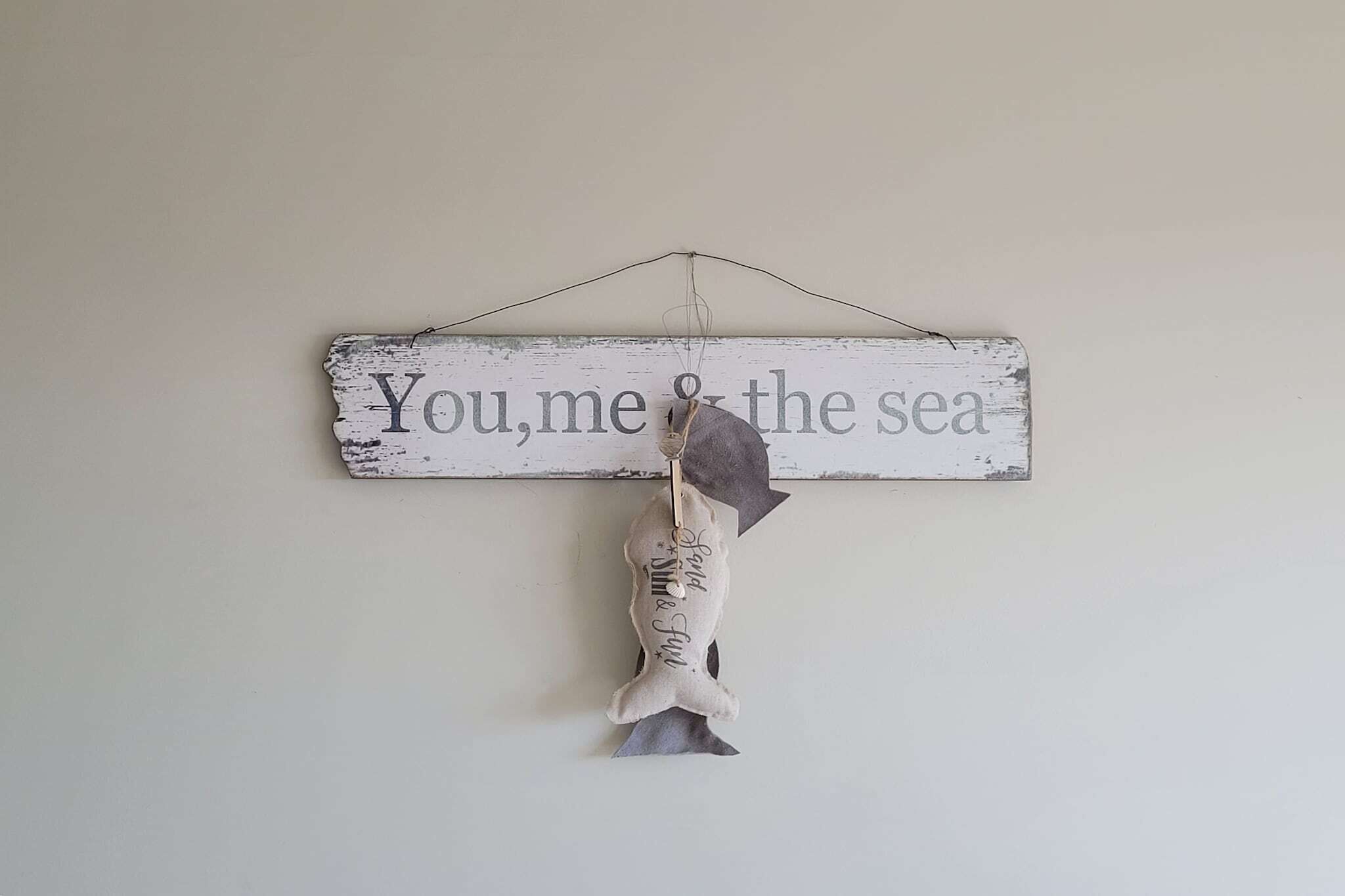 Un letrero rústico con la inscripción "You, me & the sea" colgado en una pared.