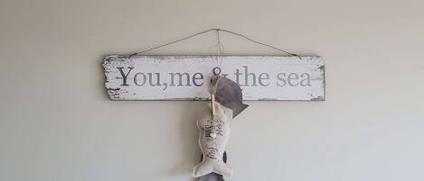 Un letrero rústico con la inscripción "You, me & the sea" colgado en una pared.