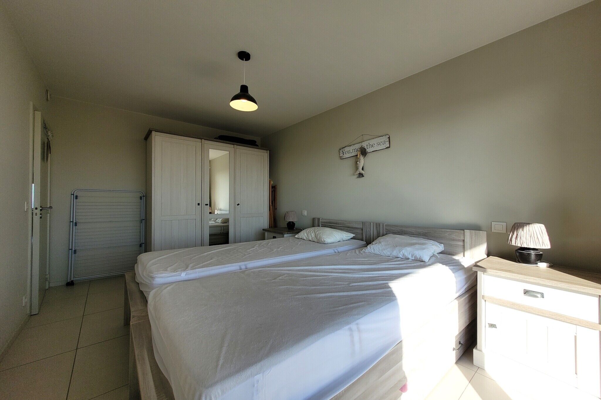 A bedroom with a bed, a nightstand, a lamp, a wardrobe, and a sign on the wall.