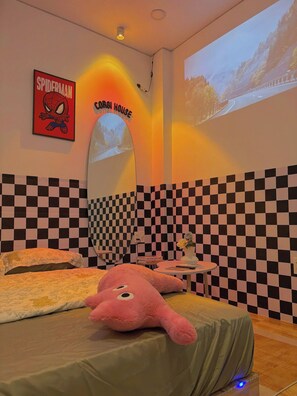 A bedroom with a checkered wall, a bed with floral bedding, a pink plush toy, a Spider-Man poster, and a projection of a scenic road.