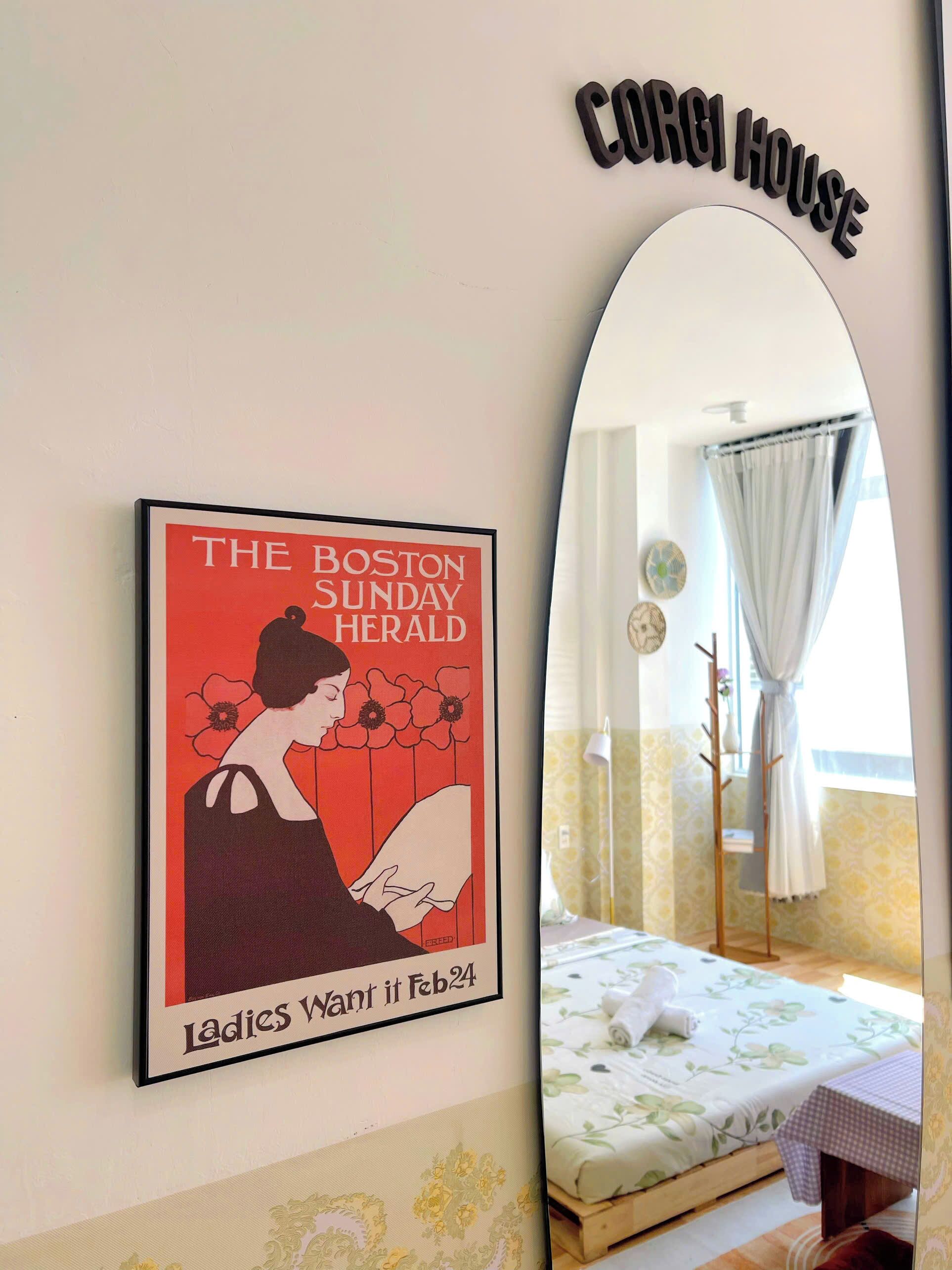 Un cartel enmarco del 'The Boston Sunday Herald' con la fecha '24 de febrero' y una habitación con una cama, una mesa y un espejo que refleja una ventana con cortinas.