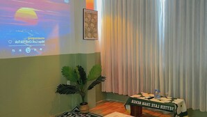 A hotel room with a bed, a projector screen displaying a movie, a potted plant, a table with a water bottle, and a curtain. - Corgi House Homestay Nha Trang 2 (Nha Trang)