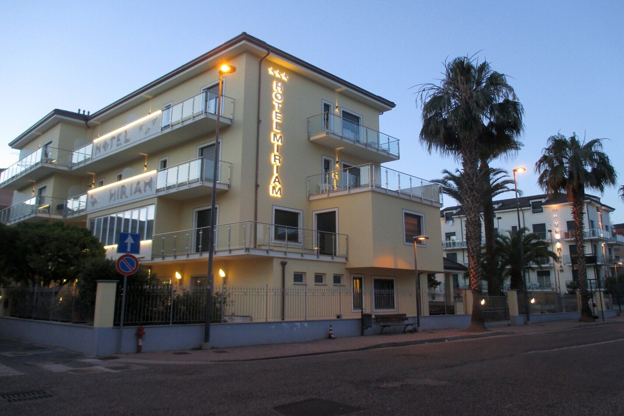 A multi-story hotel with balconies, a sign indicating it is a hotel, and a no parking sign.