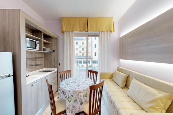 Eine kleine Küche mit Mikrowelle, Spüle und Holzausbau. Ein Esstisch mit Stühlen und eine Couch mit Kissen sind ebenfalls vorhanden.