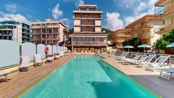 Zona de piscina con agua cristalina, rodeada de tumbonas y sombrillas, con edificios al fondo.