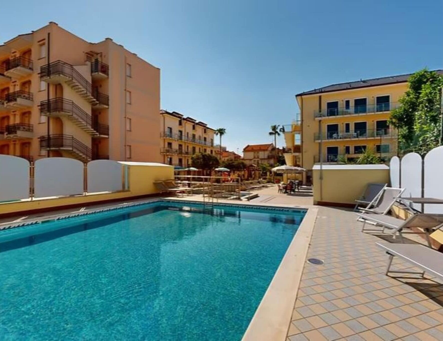 Una piscina con borde de baldosas, rodeada de edificios de varios pisos con balcones.
