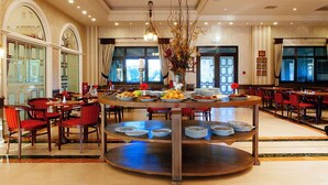 A spacious dining area with multiple round tables, red chairs, and a central decorative piece. - AIGES MELATHRON (Veroia)