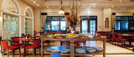 A spacious dining area with multiple round tables, red chairs, and a central decorative piece.