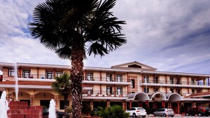 A hotel with a fountain, palm trees, and a parking lot with cars. - AIGES MELATHRON (Veroia)
