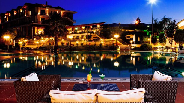 A poolside area with wicker chairs and a view of a building with multiple balconies. - AIGES MELATHRON (Veroia)
