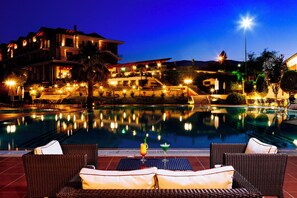 A poolside area with wicker chairs and a view of a building with multiple balconies. - AIGES MELATHRON (Veroia)