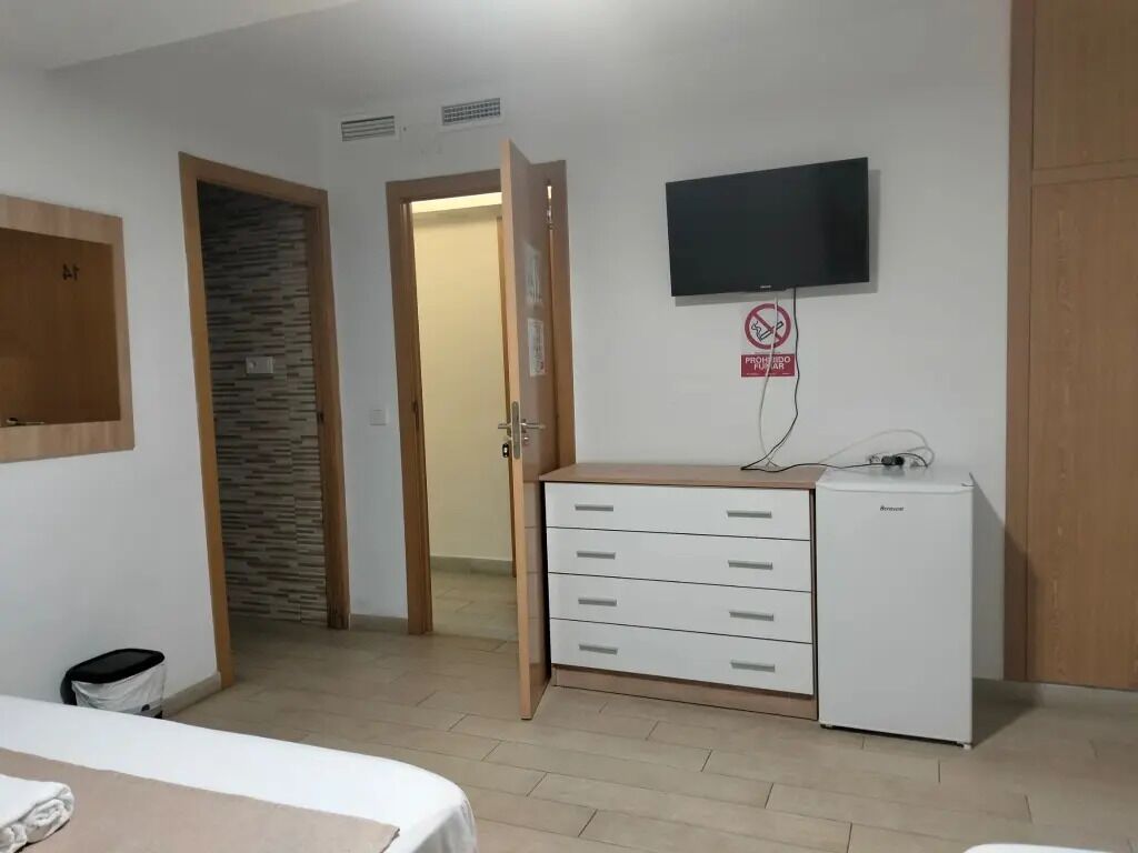 Ein Hotelzimmer mit einem Bett, einem kleinen weißen Schrank, einem an der Wand befestigten Fernseher und einer Tür zu einem weiteren Raum.
