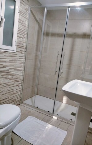 A bathroom with a toilet, a sink, a glass shower enclosure, and a tiled floor. - Pension Portugal Alicante (Alicante)
