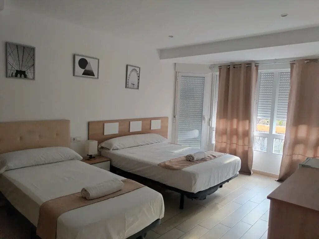 A hotel room with two beds, a window with curtains, and artwork on the wall.
