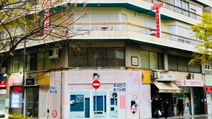 Un edificio de varios pisos con un letrero que dice 'Hotel Portugal', un paso de peatones y escaparates con varios anuncios.