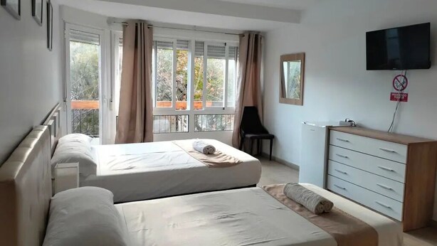 Habitación de hotel con dos camas, televisión, cómoda y balcón con cortinas.