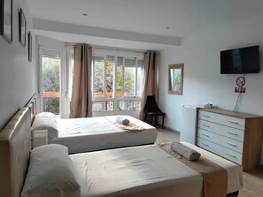 A hotel room with two beds, a TV, a dresser, and a balcony with curtains. - Pension Portugal Alicante (Alicante)