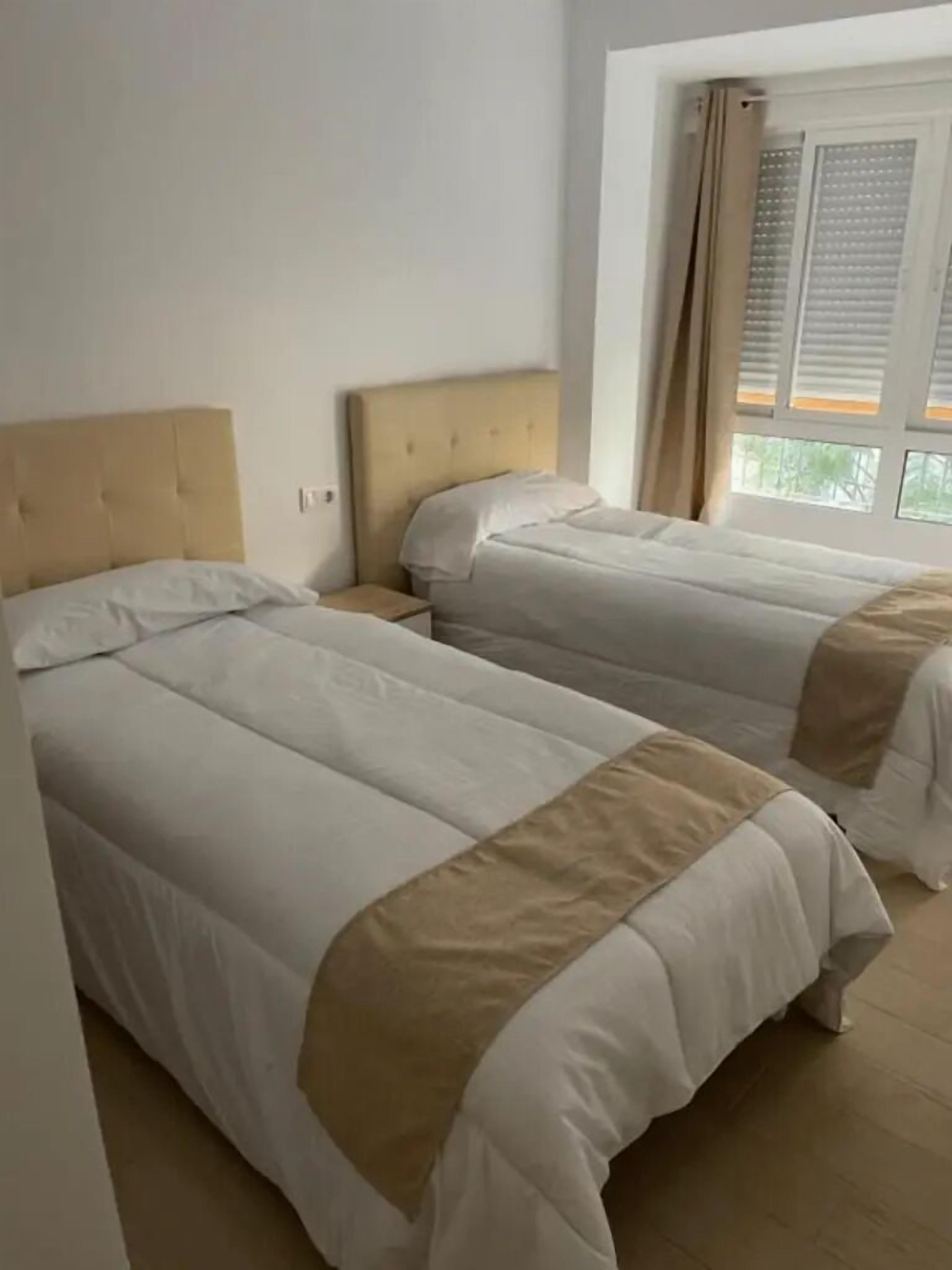 A hotel room with two beds, a window with curtains, and a view of greenery outside.