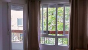 Habitación de hotel con cama, una silla, ventana con cortinas y vista a la vegetación.