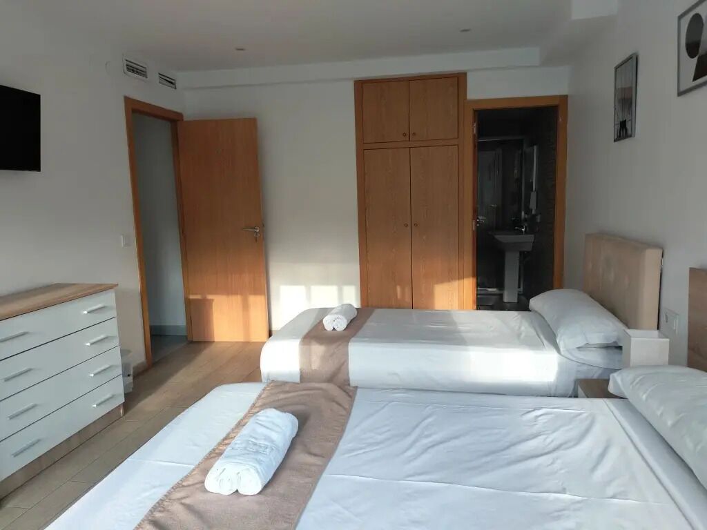 Habitación de hotel con dos camas, un armario de madera, un baño con lavabo y un televisor en la pared.