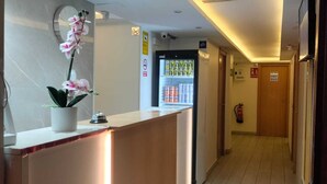 Zona de recepción de hotel con un mostrador, un reloj, señal de wi-fi y un refrigerador lleno de bebidas.