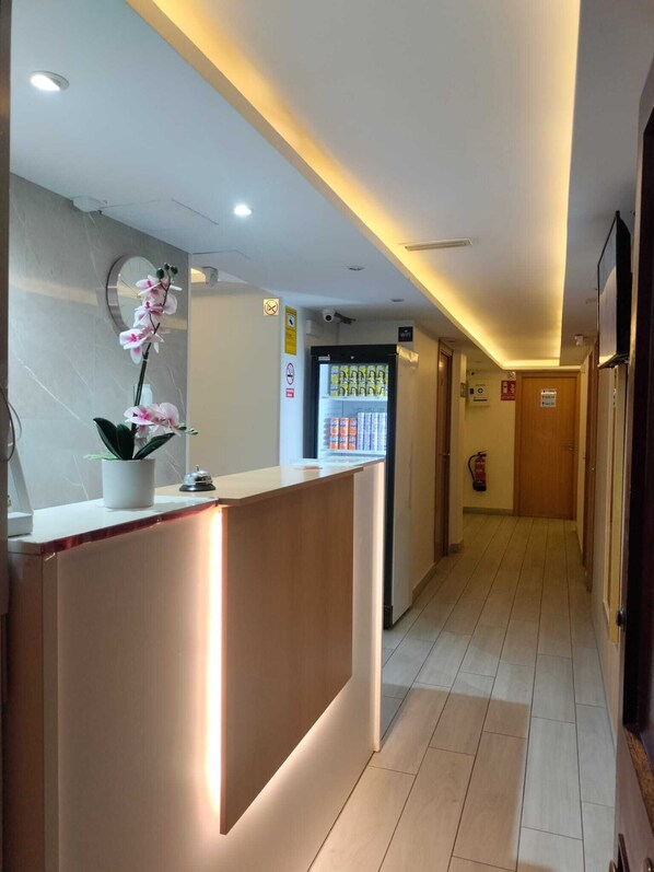 A hotel reception area with a reception desk, a clock, a wi-fi sign, and a refrigerator stocked with beverages. - Pension Portugal Alicante (Alicante)