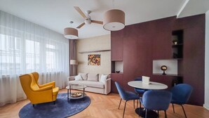 A modern living room with a sofa, yellow armchair, blue chairs, a coffee table, and a ceiling fan.