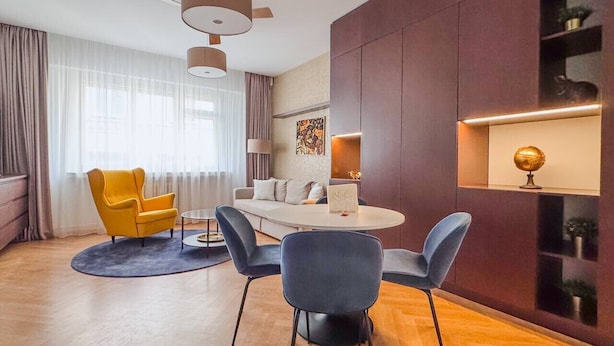 A modern hotel room with a dining area, a sofa, and a decorative wall shelf.