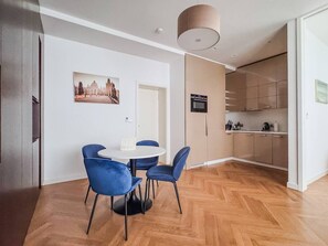 A modern kitchen with a built-in oven and microwave, a dining area with a round table and blue chairs, and a wooden herringbone floor.