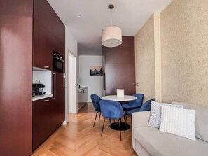 Un espacio habitable compacto con kitchenette, un área de comedor con sillas azules y un sofá con cojines.