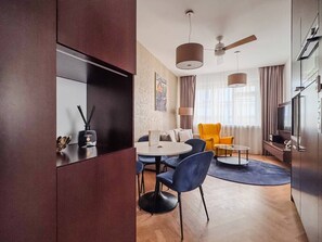 Una sala de estar moderna con una mesa redonda, sillas azules, un sillón amarillo y un televisor.